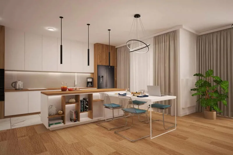 Jasny salon z aneksem kuchennym. Po lewej stronie białe szafki kuchenne, na środku wyspa kuchenna biało brązowa. Na środku biały stół i cztery niebieskie krzesła. Dużo roślina w brązowej donicy. Podłoga drewniana. Trzy podłużne, wiszące czarne lampy. Po prawej stronie trzy duże szare kotary oraz dwie firanki.