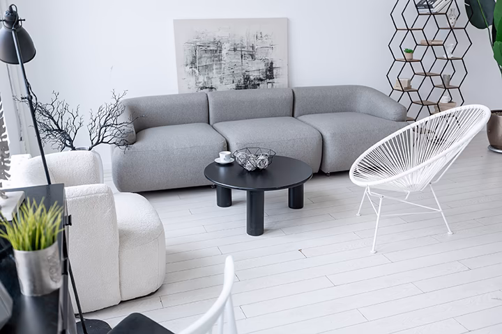 Nowoczesny salon z szarą sofą i białymi fotelami w minimalistycznym stylu.