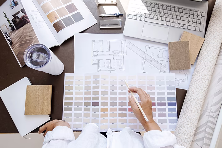 Architekt wnętrz wybiera kolory przy planach technicznych i laptopie.
