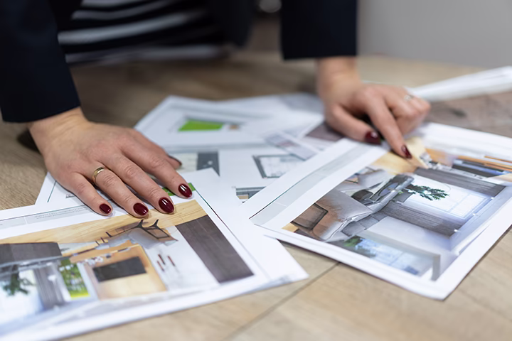 Architekt wnętrz przeglądający wydrukowane wizualizacje projektów na drewnianym stole.