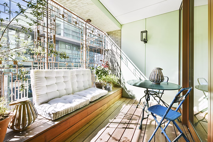 Nowoczesny balkon z drewnianą podłogą, wygodnymi poduchami i zielenią.