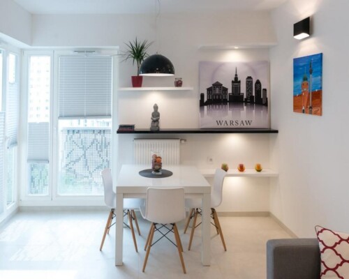 Jasna jadalnia z nowoczesnym oświetleniem i grafiką miejską – funkcjonalna przestrzeń w apartamencie Jadalnia w stylu minimalistycznym z białym stołem, krzesłami i dekoracją z panoramą Warszawy