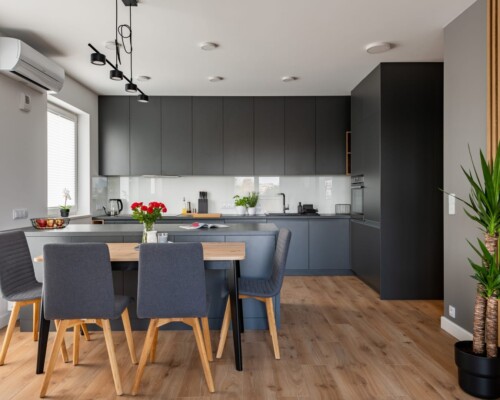 Nowoczesna kuchnia – ciemna elegancja i ciepłe wykończenie Nowoczesna kuchnia z czarną zabudową, jasnym blatem i drewnianą podłogą