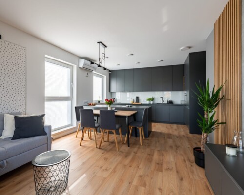 Kuchnia z pełnym potencjałem – styl i przechowywanie Nowoczesna kuchnia z wysoką zabudową, ciemnymi frontami i jadalnią w tle