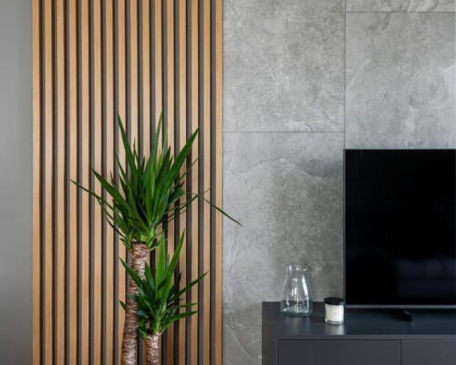 Stylowy kącik telewizyjny – elegancka aranżacja wnętrz z naturalnymi akcentami Nowoczesny salon z betonową ścianą, lamelami drewnianymi i rośliną doniczkową – aranżacja wnętrz mieszkania