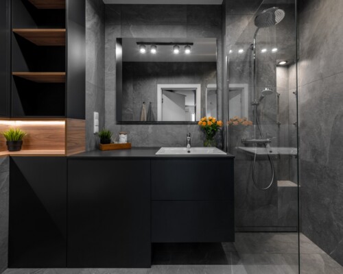 Mocny akcent w łazience – czerń, drewno i światło Nowoczesna łazienka z czarną zabudową, drewnem i podświetlanym lustrem